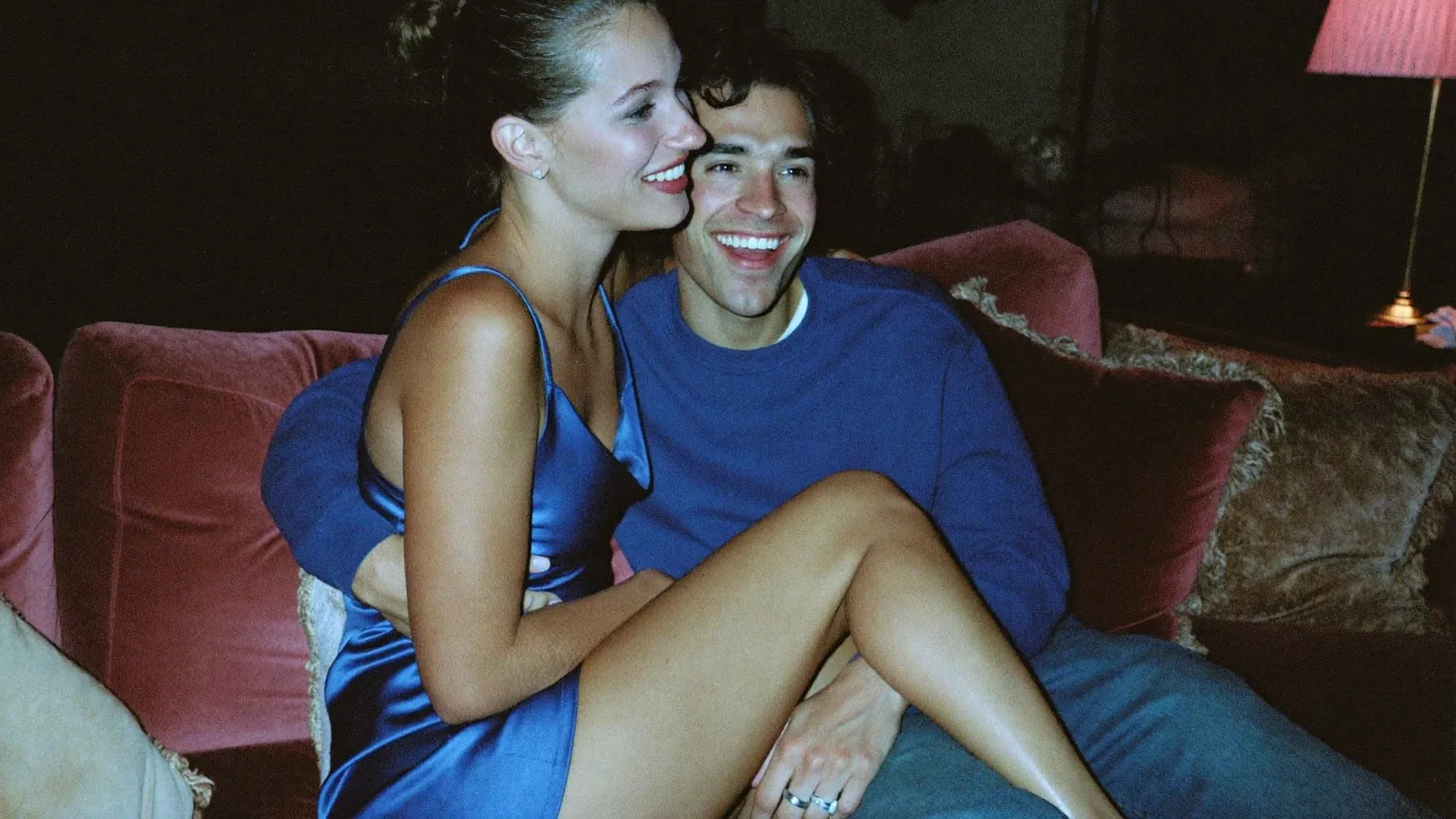 Couple cuddling on a velvet sofa, she wears a blue satin dress