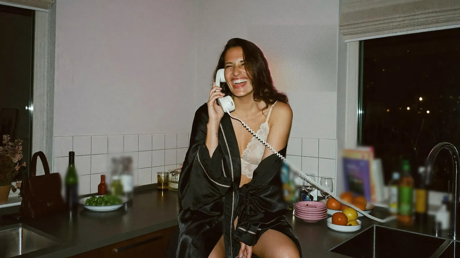 Cam model in a satin robe laughing on the phone in her kitchen