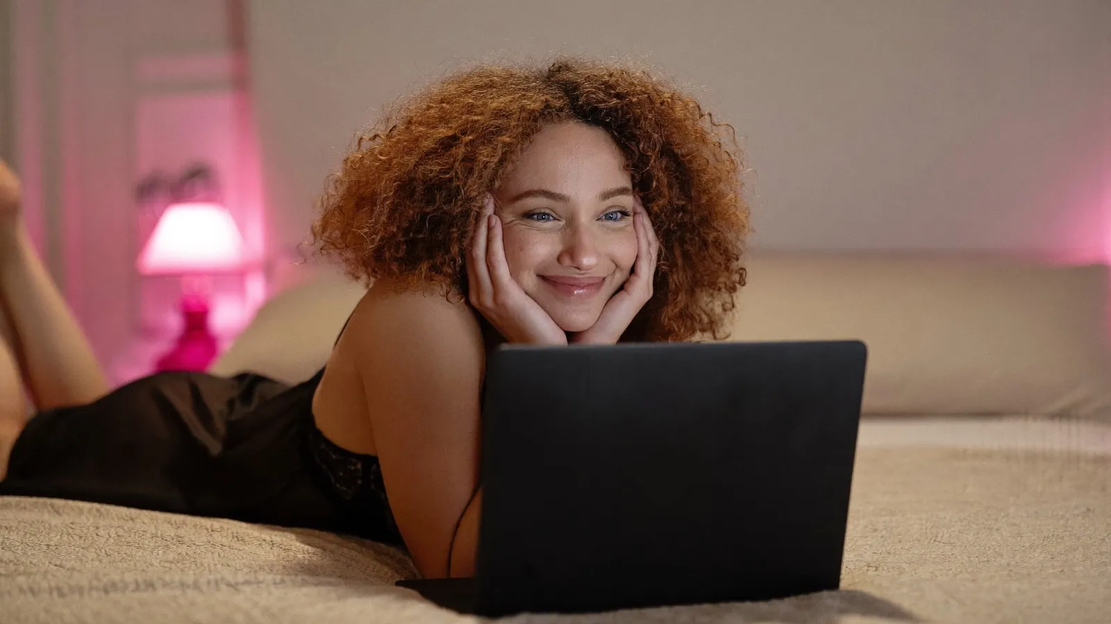Curly-haired cam model smiling over her laptop
